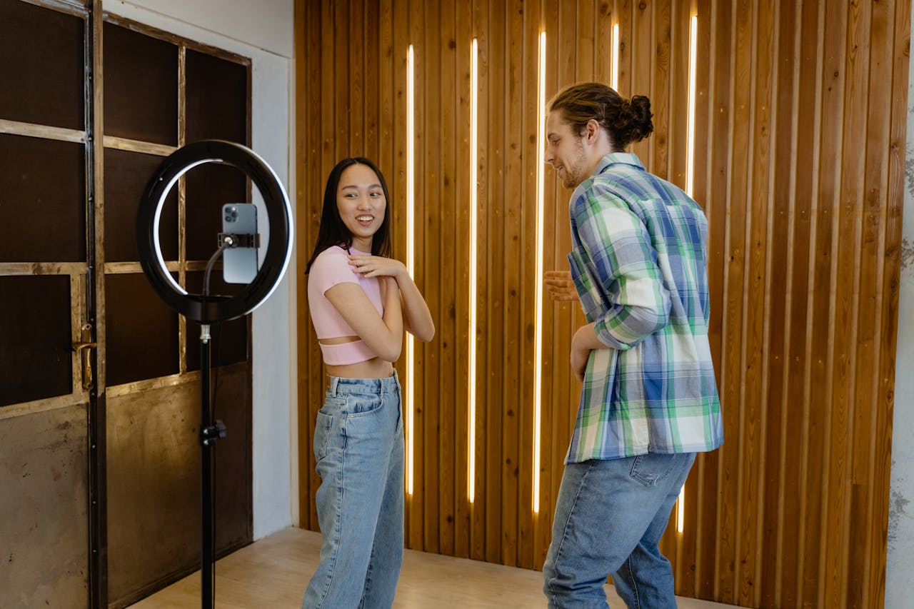 Two young adults having fun dancing in front of a phone camera indoors.
